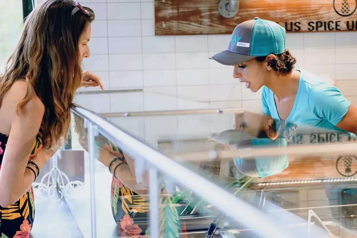 A customer at Bolay Fresh Bold Kitchen ordering from a staff member in a blue hat behind the counter